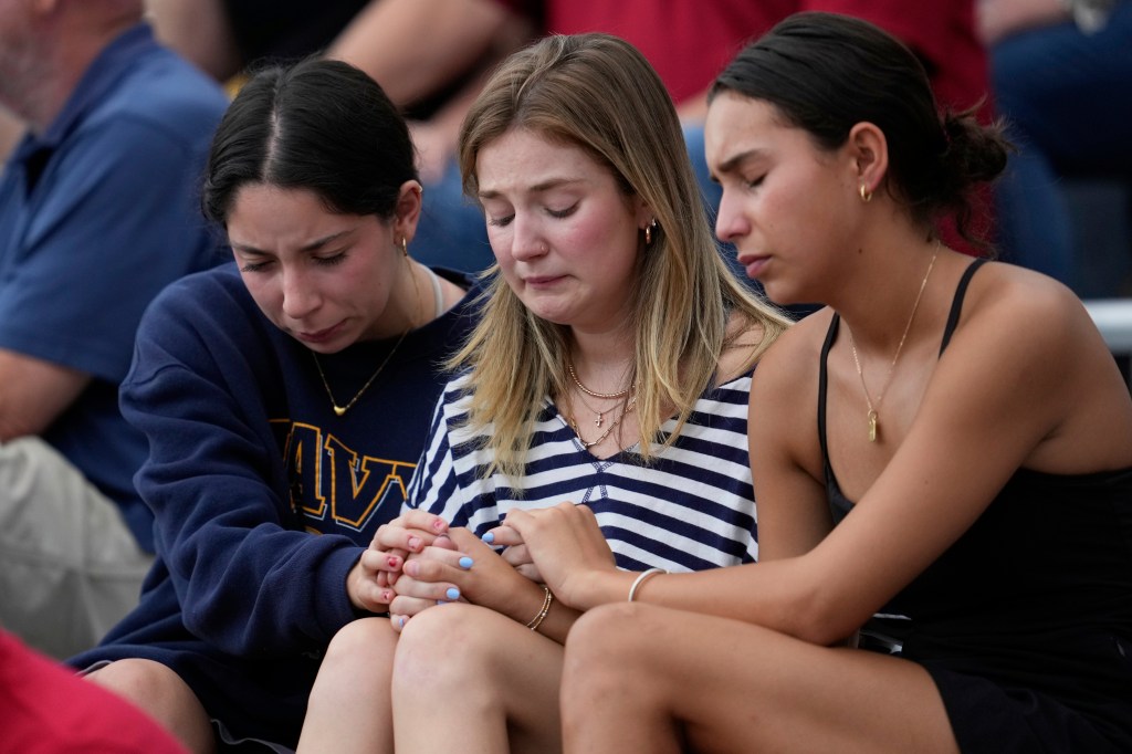 Three women praying together at a vigil for flood victims.